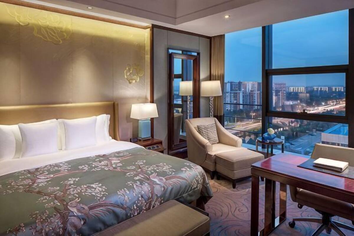 A hotel room with a large bed, a desk, a chair, and a view of a cityscape.