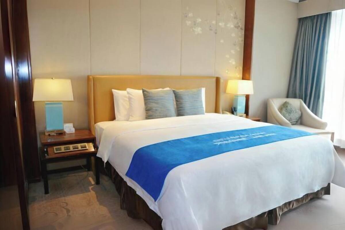 A hotel room with a large bed, two bedside tables with lamps, a chair, and a view of the outdoors.