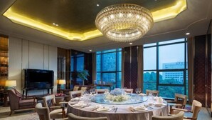 Ein luxuriöser Speisesaal mit einem runden Tisch, gedeckt für sechs Personen, umgeben von bequemen Stühlen. Eine große Chandelüster hängt von der Decke, und das Zimmer verfügt über große Fenster mit Blick auf die Stadtlandschaft.