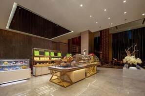 Un vestíbulo moderno de hotel con una zona de bufé central, una recepción y un gran ventanal.
