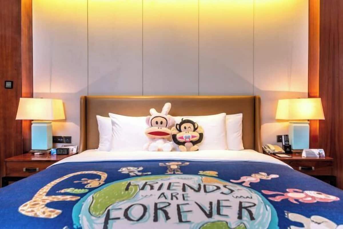 Ein Hotelzimmer mit einem Bett, das mit einem Bettbezug im 'Friends are Forever'-Design ausgestattet ist, zwei Nachttischen mit Lampen und einem Holz-Kopfbrett.