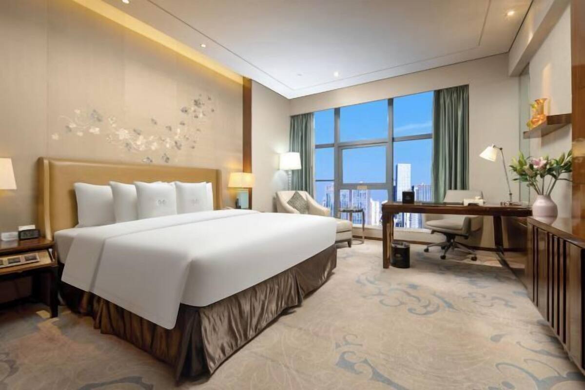 A hotel room with a large bed, a desk, a chair, and a view of the city.