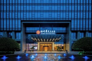 Un moderno edificio de hotel con una entrada amplia, señalización iluminada y una fuente en la parte frontal.