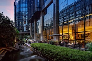 Un hotel moderno con terraza exterior, fuente de agua y fachada bien iluminada.