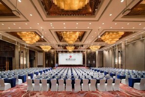 Une salle de conférence avec des rangées de chaises, une scène dotée d’un écran et un lustre.