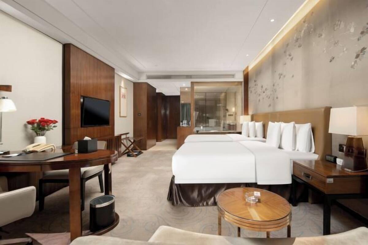 A hotel room with a large bed, a desk with a chair, a TV, and a small table.