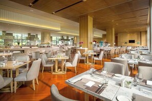 A spacious dining area with multiple tables and chairs, large windows, and a modern interior design.