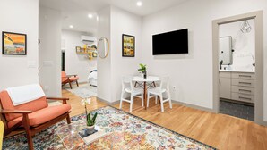 A modern living room with a sofa, a coffee table, a TV, and a dining area with chairs and a table. - Cozy studio, Pet Friendly, Outdoor Oasis near Zilker  (Austin)