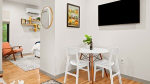 A modern living room with a white sofa, a dining table with white chairs, a flat-screen TV, a framed picture, and a small plant on the table. - Cozy studio, Pet Friendly, Outdoor Oasis near Zilker  (Austin)