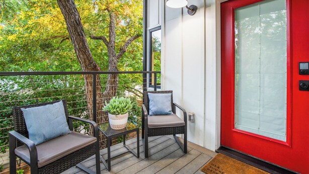 A balcony with two wicker chairs, a small table with a plant, and a red door. - Cozy studio, Pet Friendly, Outdoor Oasis near Zilker  (Austin)