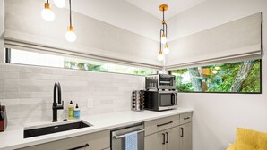 A modern kitchen with a built-in microwave, a sink, and a dishwasher. There is a window with a view of greenery outside. - Cozy studio, Pet Friendly, Outdoor Oasis near Zilker  (Austin)