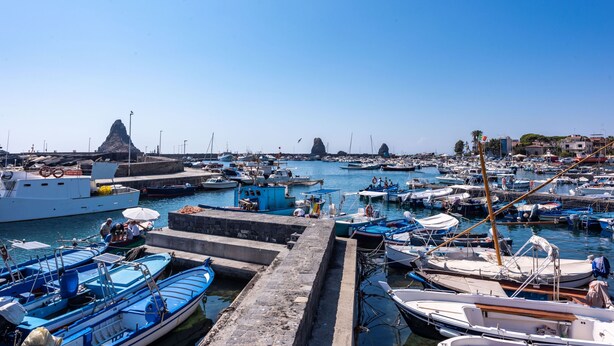 Un port de plaisance où sont amarrés différents types de bateaux, un ciel dégagé et, au loin, une formation rocheuse.