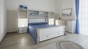 Une chambre à coucher comprenant un lit, des rangements intégrés, une commode, un miroir et une fenêtre avec des rideaux.