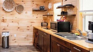 Eine kleine Küche mit Holzwänden, einem Spülbecken, einer Mikrowelle und einer Kaffeemaschine.