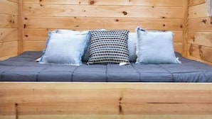 Ein holzgetäfelter Raum im Blockhausstil mit einem Bett, Kissen und einem Maschendrahtzaun.