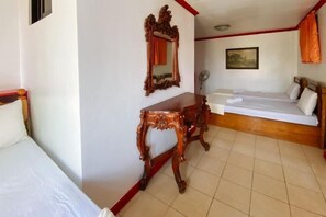 A hotel room with a bed, a wooden dresser, a mirror, a painting on the wall, and a fan. - RedDoorz Hostel @ Tita Aidz Inn Baguio (Baguio)