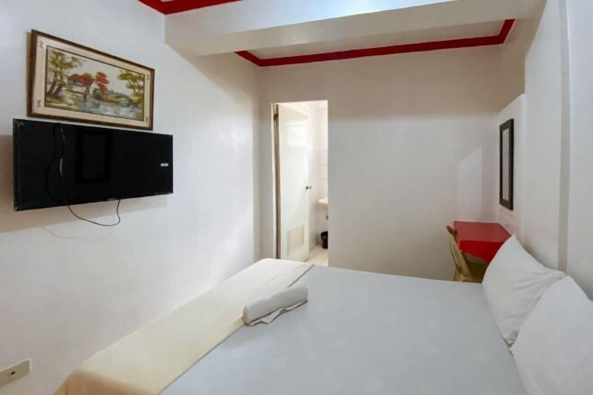 A hotel room with a bed, a TV mounted on the wall, and a door leading to another room.