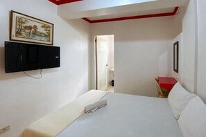 A hotel room with a bed, a TV mounted on the wall, and a door leading to another room. - RedDoorz Hostel @ Tita Aidz Inn Baguio (Baguio)