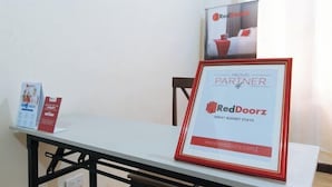A framed RedDoorz partnership sign on a table with brochures and a RedDoorz poster in the background. - RedDoorz Hostel @ Tita Aidz Inn Baguio (Baguio)