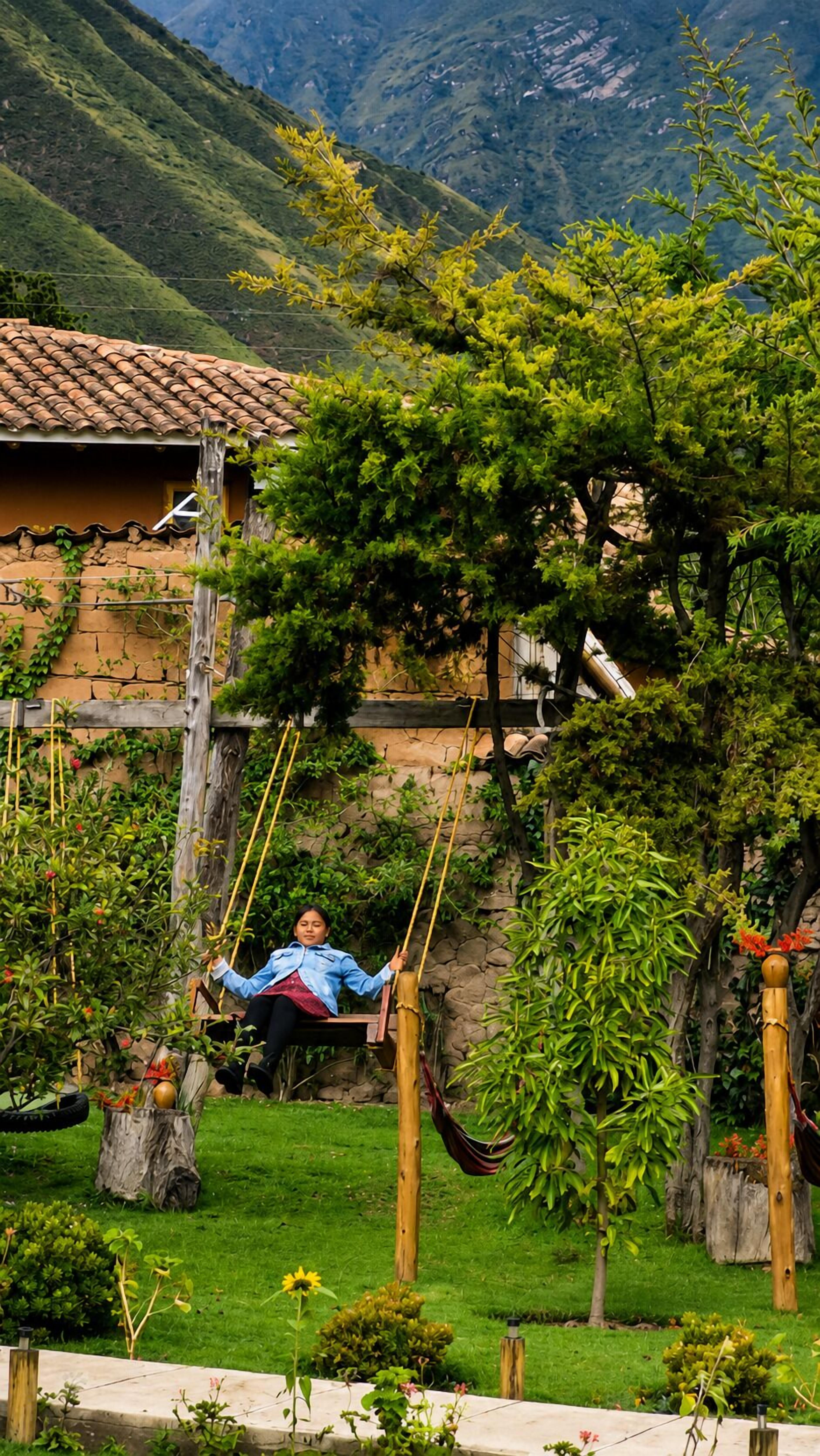 Una persona sentada en una hamaca en un jardín exuberante, con montañas al fondo.