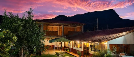 A two-story house with a patio, a covered outdoor seating area, and a mountain backdrop.