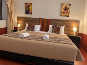 A hotel room with a large bed, two nightstands, a headboard with a patterned design, and two wall-mounted paintings. - Chaska Valle Green (Urubamba)