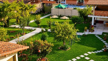 Un patio con un sendero pavimentado, un árbol pequeño y una sombrilla verde.