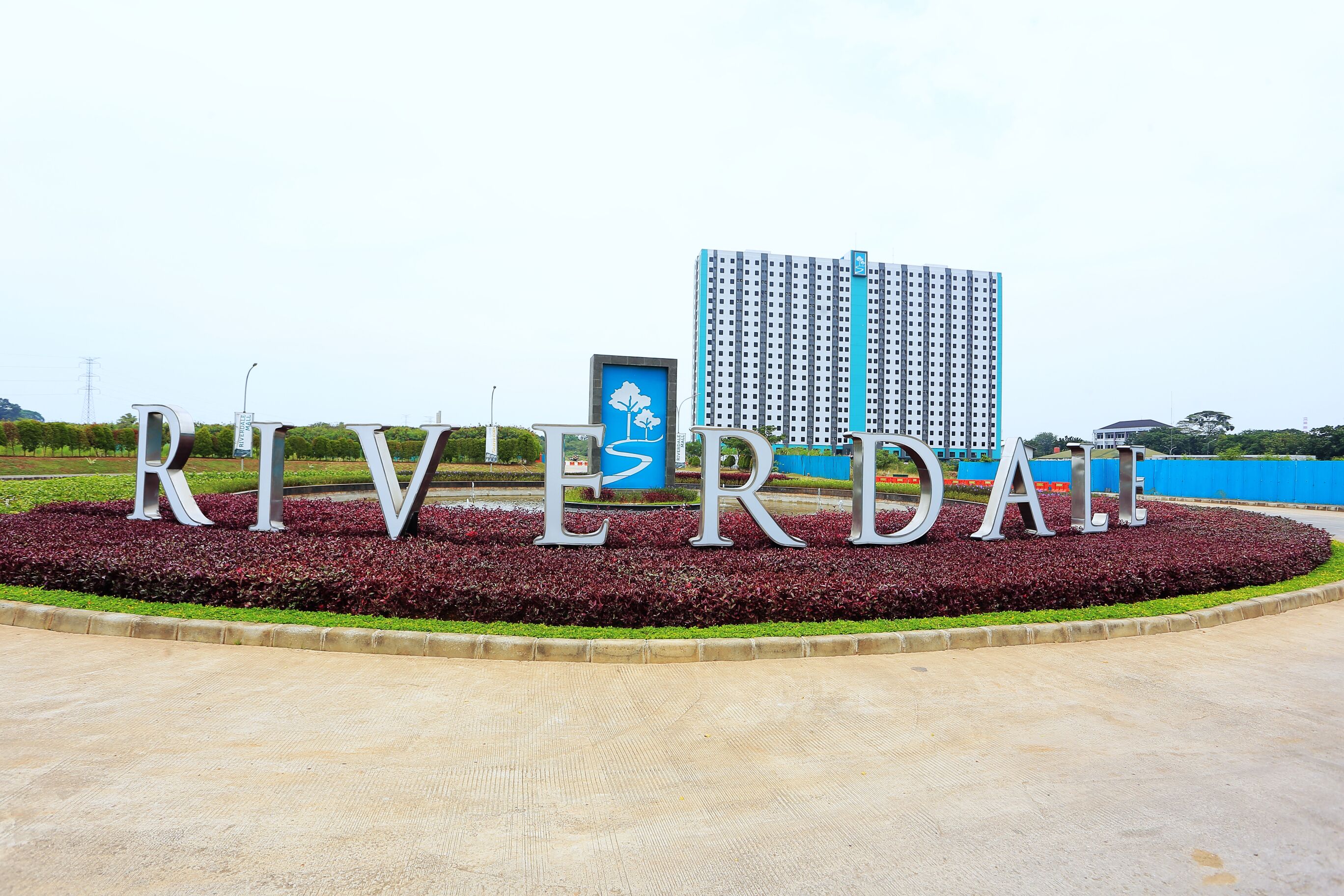 A large sign with the word "RIVERDALE" in metallic letters, surrounded by a landscaped area with red and green plants.