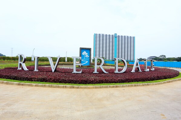 Un letrero grande con la palabra 'RIVERDALE' en letras metálicas, rodeado por un área ajardinada con plantas rojas y verdes.