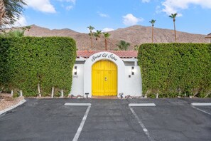 A building with a yellow door, surrounded by greenery and a mountainous backdrop. - Spirit of Sofia (Palm Springs)