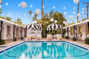 A swimming pool with lounge chairs and umbrellas, surrounded by palm trees and a clear sky. - Spirit of Sofia (Palm Springs)