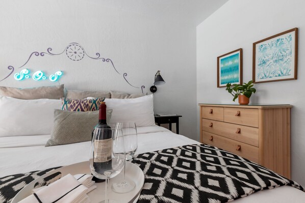A neatly arranged bedroom with a bed, pillows, a bedside table with a lamp, a dresser, and two framed artworks on the wall. - Spirit of Sofia (Palm Springs)