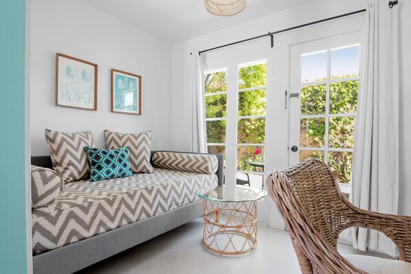 A modern living room with a grey sofa, patterned cushions, a glass coffee table, and a wicker chair.