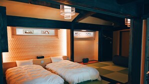 A traditional Japanese-style room with tatami flooring, a low wooden ceiling, and a shoji screen door. There are two beds with white bedding and a small table between them. - Cocon Setouchi (Suooshima)