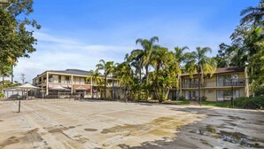 A multi-story hotel with outdoor seating, palm trees, and a parking lot. - Spacious Room Ideal for Biz District & Access CBD (Mount Ommaney)