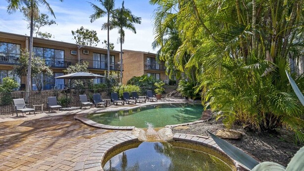 A pool area with lounge chairs, a hot tub, and a building with multiple windows and balconies. - Spacious Room Ideal for Biz District & Access CBD (Mount Ommaney)