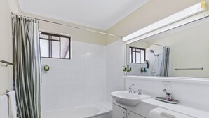 A bathroom with a bathtub, a sink, a mirror, and a shower curtain. - Spacious Room Ideal for Biz District & Access CBD (Mount Ommaney)