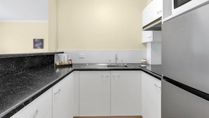 A modern kitchen with white cabinets, a black countertop, and a stainless steel refrigerator. - Suite with Kitchen, WiFi & Easy Access to Motorway (Mount Ommaney)