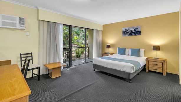 A hotel room with a bed, bedside tables, a desk, a chair, and a balcony with a view of greenery. - Suite with Kitchen, WiFi & Easy Access to Motorway (Mount Ommaney)