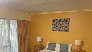 Une chambre d’hôtel avec un grand lit, deux tables de chevet, une fenêtre avec des rideaux et une œuvre d’art accrochée au mur.