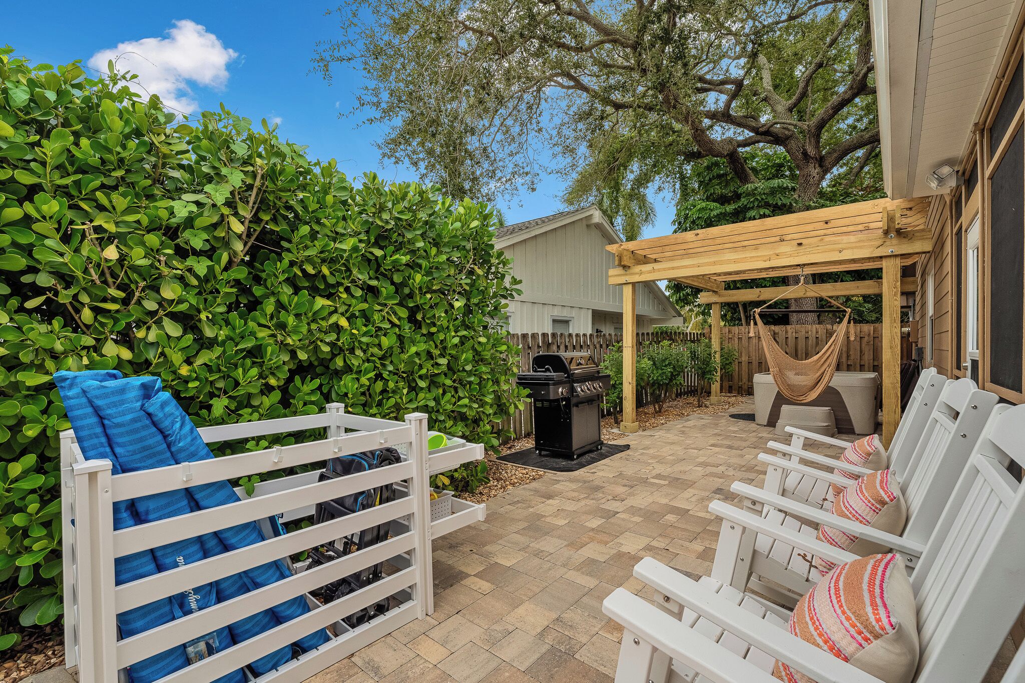 Une terrasse avec des chaises blanches, un hamac et un barbecue.
