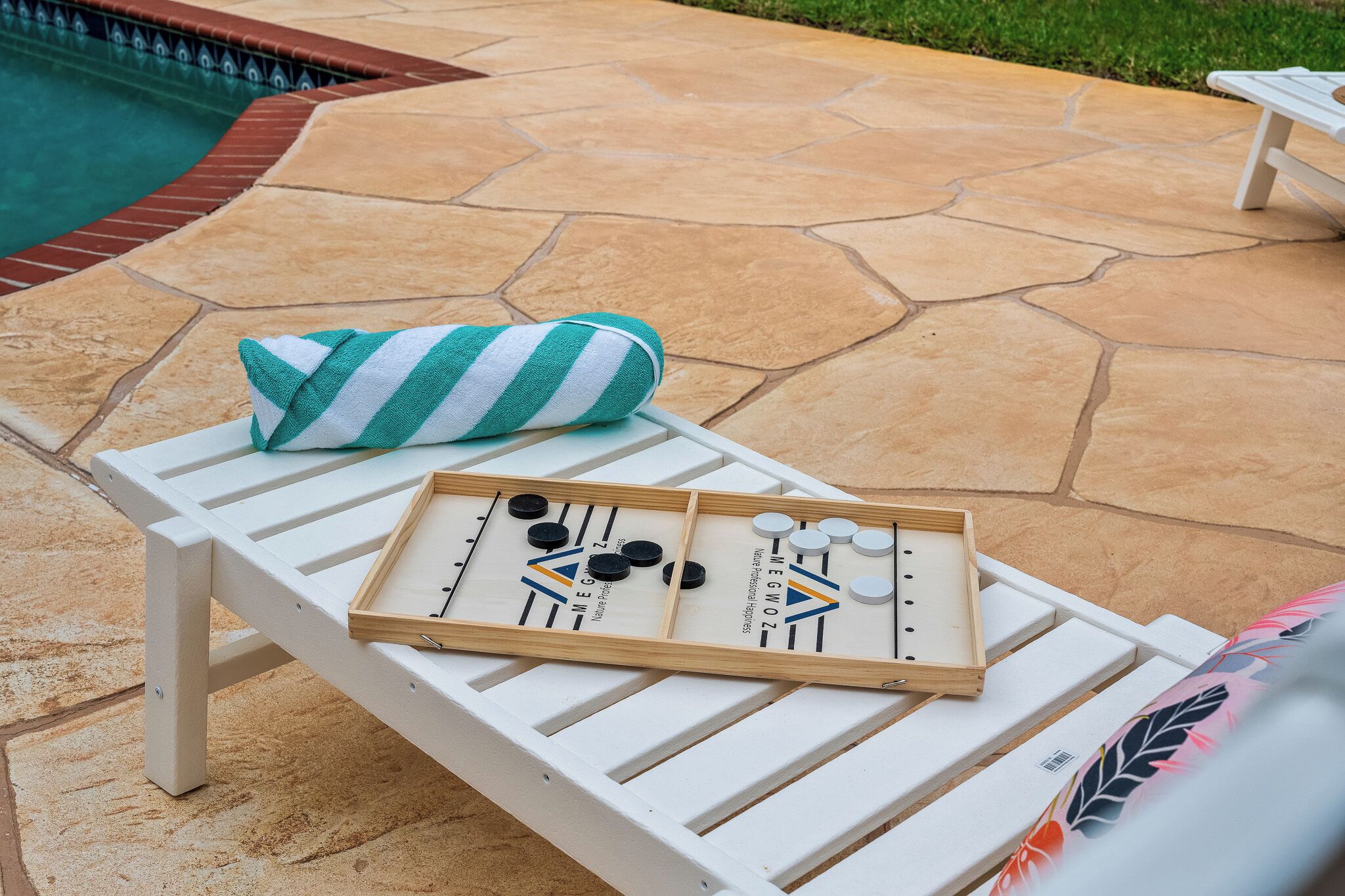 A poolside area with a white lounge chair, a striped towel, and a shuffleboard table.