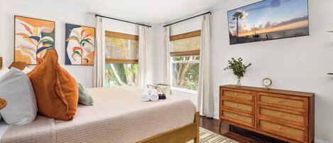 A bedroom with a bed, a wooden dresser, a TV, and artwork on the walls.