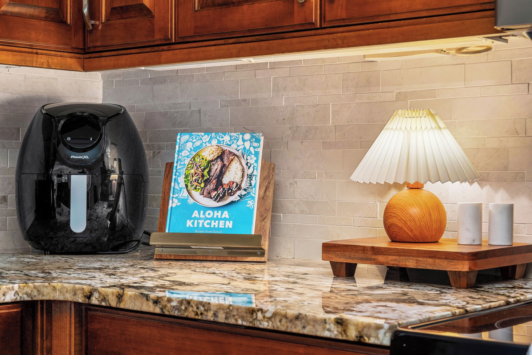 A kitchen with a coffee maker, a framed recipe book, and a table lamp.