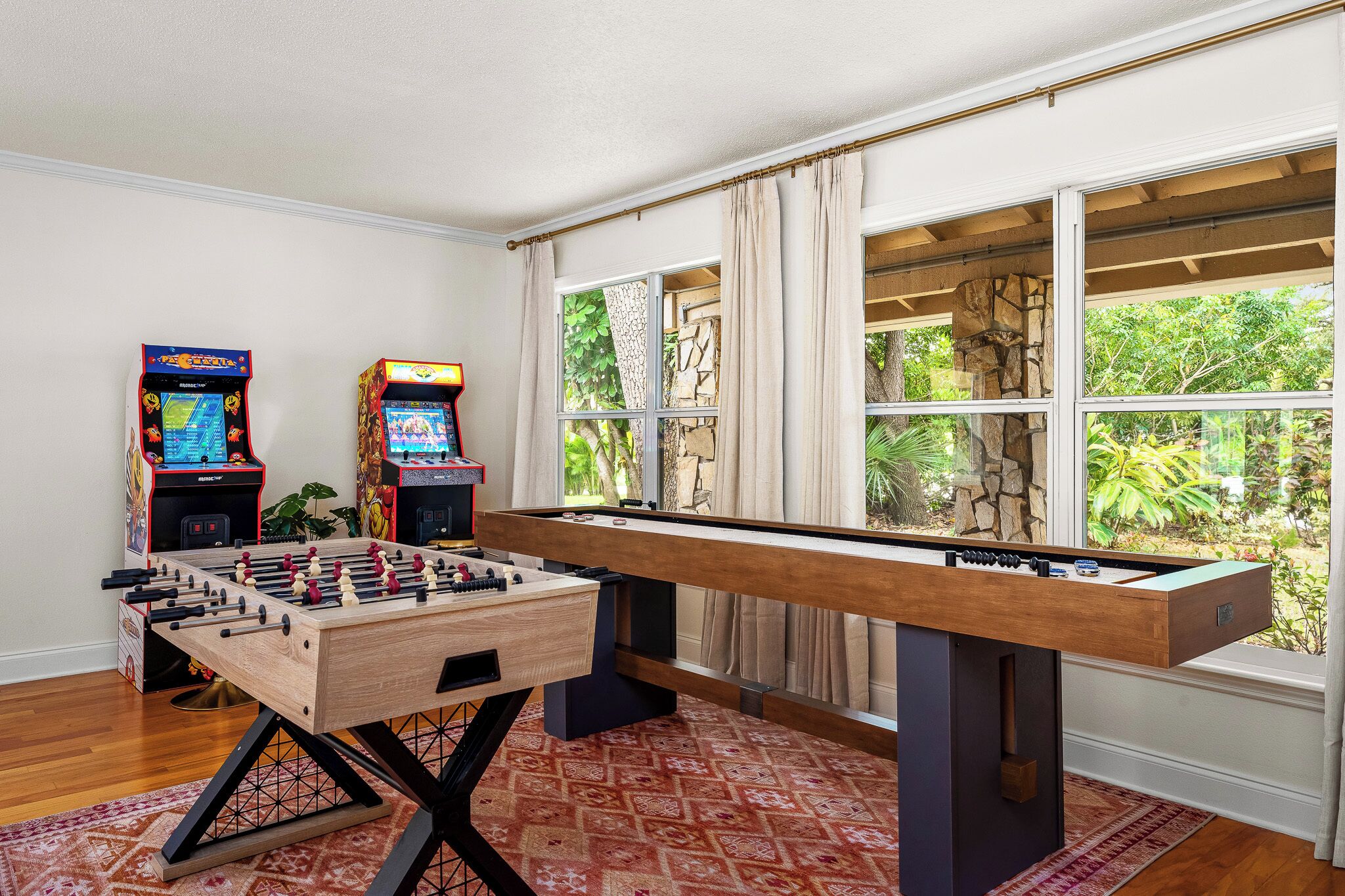 Una habitación con mesa de fútbol, dos máquinas de arcade y un ventanal con vistas a zonas verdes.