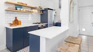 Una cocina moderna con armarios azul oscuro, una encimera blanca y un horno empotrado. Hay estantes de madera sobre la encimera con vajilla y vasos.