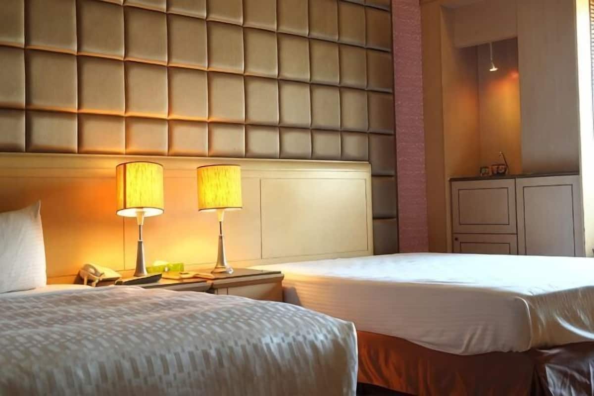 Una habitación de hotel con dos camas, cabecera acolchada, lámparas de noche, teléfono y armario.