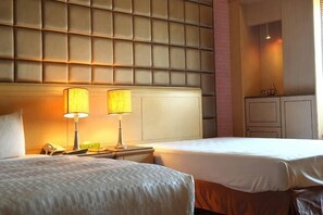 Una habitación de hotel con dos camas, cabecera acolchada, lámparas de noche, teléfono y armario.