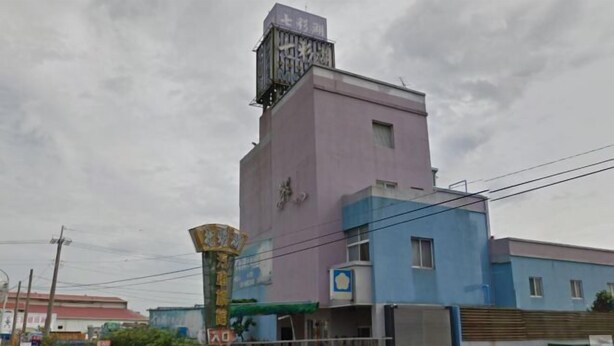 Un edificio a più piani con una torre evidente, una targa e una facciata blu e rosa.