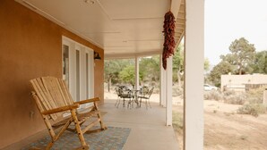 Een overdekte veranda met twee houten schommelstoelen, een decoratief vloerkleed en een hangende decoratie.